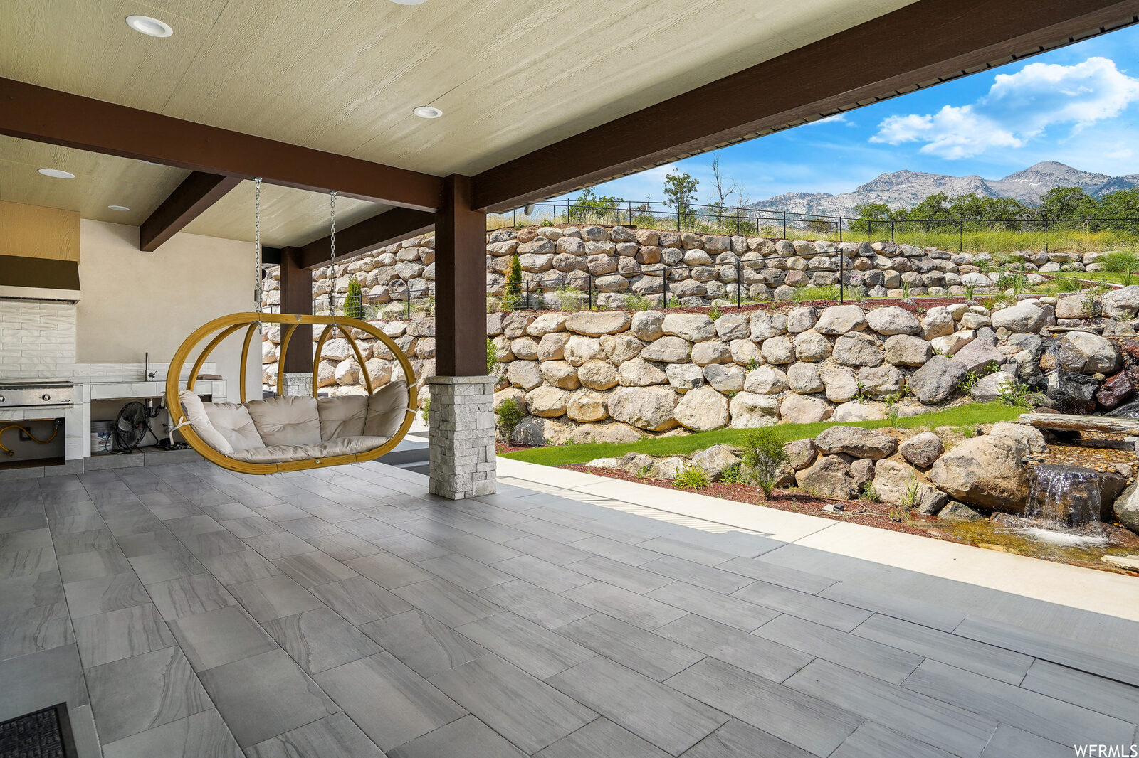 Covered patio with outdoor kitchen and rock-wall backdrop